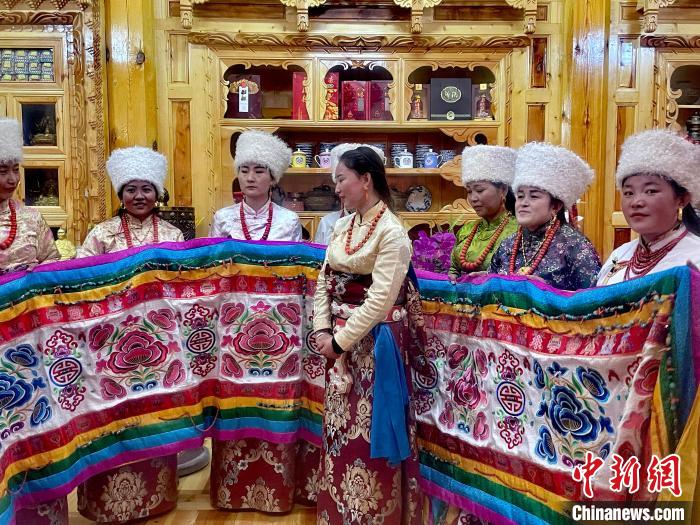 圖為女性展示村民自發(fā)繡制的“百米五彩哈達(dá)”?！±钣穹?攝